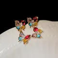 Detailed macro view of vibrant colorful zircon butterfly drop earrings with gold plating. - Colorful