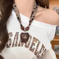 Close-up detail of a leopard print scarf necklace featuring a wooden heart pendant - Necklace Style 24 / Brown