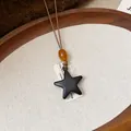 Primo piano di un ciondolo a stella in resina nera su un cordino marrone con perla - Ciondolo a Stella (6098608443391)