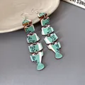 Dettaglio di orecchini pendenti in legno a forma di lisca di pesce colorata - Stile a Gancio / Verde Macchiato