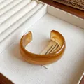 Elegant amber resin cuff bracelet with irregular swirl pattern displayed in a tray - Style 59