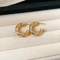 Elegant gold twisted C-shaped stud earrings displayed on a soft cream velvet tray - Style 17 / Gold