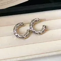 Close-up detail of silver C-shaped hoop earrings with hammered texture on cream fabric - Style 16 / Silver