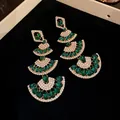 Macro detail of emerald green fan-shaped drop earrings with sparkling rhinestone accents. - Earrings / Green