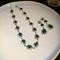 Detailed view of elegant emerald green teardrop necklace and earring set on a white plate. - Green