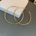 Close-up of oversized gold open hoop earrings with minimalist metallic finish - Gold