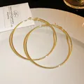Detail shot of large golden hoop earrings with a glossy metallic finish on a white plate - Shiny Gold Plain Style / 7cm / Gold