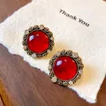 Primo piano di orecchini vintage in resina con pietra rossa e bordi dorati stile palazzo. - Oro con Rosso