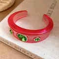Macro detail of a red translucent resin cuff bracelet featuring green oval rhinestones - Rose Red Green