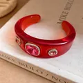 Close-up of red resin cuff bracelet with rhinestones and pink stones on a book background. - Red Rose Red