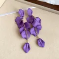 Close-up of bohemian matte purple petal tassel drop earrings on beige texture - Purple