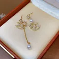 Macro view of asymmetrical rocking horse earrings with zircon and pearls in a jewelry box. - Silver Pin - Asymmetric Tassel Style / Gold