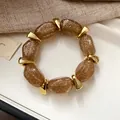 Detailed macro view of an amber glitter acrylic oval beaded bracelet with gold accents. - Light Coffee