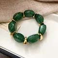Close-up of green glitter acrylic oval beaded bracelet with gold spacers on white tray. - Green