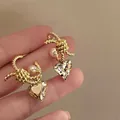 Close-up of golden twisted C-shaped earrings with pearls and heart crystals - C-Shaped Twisted Heart Pearl Style (HE25656) / Gold