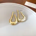 Primer plano de pendientes geométricos dorados en forma de U sobre un plato blanco - Forma de U Retorcida / Dorado