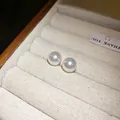 Primer plano de pendientes de perlas blancas redondas en un joyero de color crema suave. - 10mm / Blanco