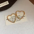 Close-up of minimalist gold-plated heart-shaped hoop earrings on fabric background - Large / Gold
