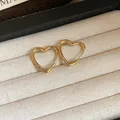 Close-up of minimalist gold-finished heart-shaped hoop earrings on white texture - Small / Gold