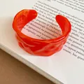 Primo piano di un bracciale rigido retrò in acrilico arancione con trama ondulata unica - Bracciale #2 - Rosso Rosa