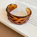 Macro di un bracciale a polsino in acrilico ambra con trama increspata su un libro. - Bracciale #9 - Ambra
