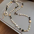 Close-up of long vintage necklace with white pearls, black beads, and gold floral charms. - Gold-White-Black