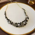 Elegante collana geometrica con strass a goccia in finitura dorata esposta su un piatto. - Collana-Nero