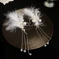 Primer plano de elegantes orejeras de plumas blancas y borlas de perlas. - Pendiente de Manguito - Blanco / Un par