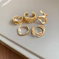 Macro view of five assorted gold irregular geometric open rings on a grey book surface - Style 1