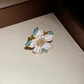 Close-up of a vintage-style white enamel flower pendant with rhinestones and turquoise accents - Ring