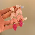 Close-up of pink raffia flower drop earrings held by hand for detail and scale - Pink Gradient Spindle Woven Style (8#)