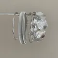 Close-up of textured silver metal bracelet set hanging on a minimalist display rod - Four-Piece Set / Silver