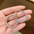 Close-up detail of silver hoop earrings featuring a textured ridge wave pattern held in hand - Diagonal Texture Round (31mm Diameter) / Silver