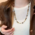 Close-up of retro coffee tiger eye stone necklace worn with a white sweater and brown jacket - Cylindrical Tiger Eye Beads (13#) / Gold & Brown Cylinder