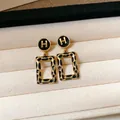 Primo piano di orecchini vintage leopardati dorati a forma rettangolare con logo H in un portagioie - 33# Oro Nero (Stile Logo H)