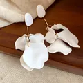 Detailed macro view of elegant white petal earrings with golden hardware on a wooden background - White