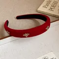 Close-up of a red velvet headband with golden bee pins in a vintage setting - Red