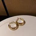 Dettaglio ravvicinato di eleganti orecchini a cerchio dorati su un piatto bianco. - Stile con perno dell'orecchino in argento / Pasta Dorata Attorcigliata