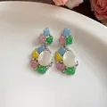 Primer plano de pendientes de resina de colores con cabujón blanco ovalado y cristales finos - Par de Pendientes / Multicolor