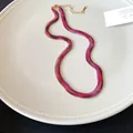 Detalle de un collar de cadena plana con estampado de serpiente sobre un plato blanco. - Rojo