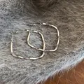 Elegant silver-colored twisted square hoop earrings presented on a soft grey fur background - Irregular Square (HE8275) / Silver