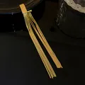 Nahaufnahme eines hochwertigen goldfarbenen Quastenohrrings mit feinen Schlangenketten auf Schwarz. - Geometrischer Schlangenknochenfransen-Stil (21#)