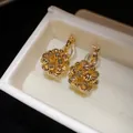 Close-up of 18k gold plated round flower cluster clip-on earrings in a white gift box - Clip-On Earrings / Gold