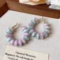 Detalle de pendientes de aro con cuentas de resina pastel y acabado dorado - Aros de Cuentas / Azul Cielo y Púrpura