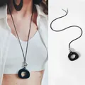 Macro view of a black resin hollow round pendant on a thin leather cord necklace - Black