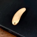 Macro dettaglio di una spilla geometrica a goccia d'oro lucido su uno sfondo nero strutturato. - Oro