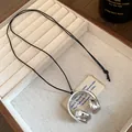 Detailed close-up of a silver-toned headphone pendant necklace on a beige jewelry display tray - Headphone / Silver
