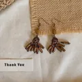 Vue détaillée de boucles d'oreilles pendantes ethniques vintage sur fond rustique. - Crochet d'oreille-perles ethniques / Marron
