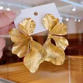 Detailed view of oversized gold ginkgo leaf metallic earrings with textured petals - Gold