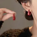 Detailed view of glossy red geometric hoop earrings worn by a model in soft lighting - Geometric Studs / Red